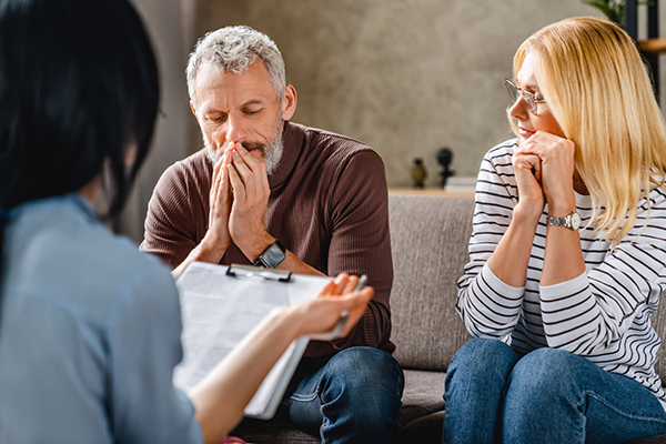 Worried middle aged couple sitting on sofa with financial advisor at home