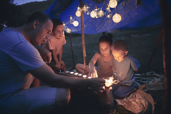 Father with children playing under their backyard tent with lanterns.