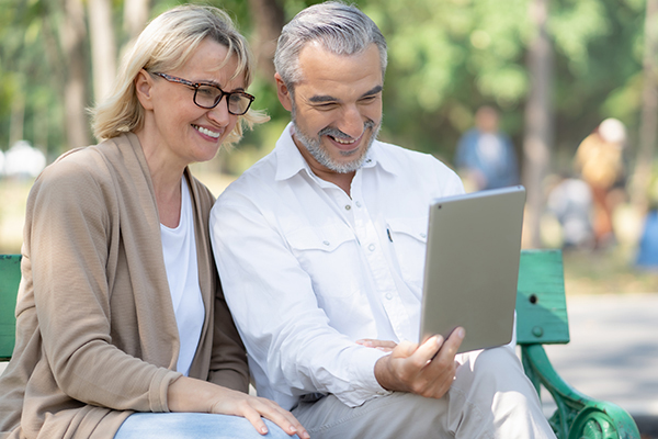 Technology connect and modern elderly lifestyles concept. Aged senior couple waving hands greeting grandkids via facetime video call internet conference outdoors in the park