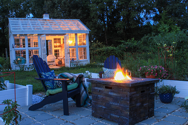 Beautiful Garden Scene at Dusk with Firepit, Andirondack Chairs and Greenhouse with lit chandelier