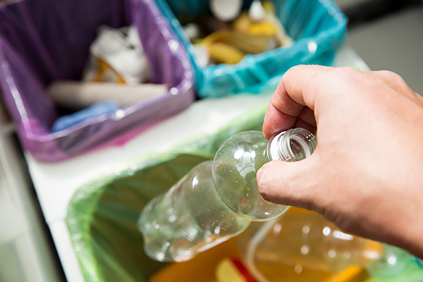 Man putting empty plastic bottle in recycling bin in the kitchen. Person in the house kitchen separating waste. Different trash can with colorful garbage bags. Top view